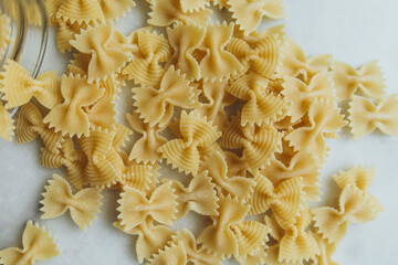 scattered raw farfalle pasta on a white marble table close-up. farfalle pasta on white background top view. butterfly pasta