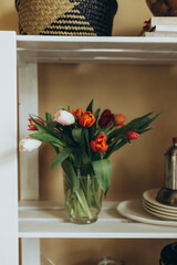 bouquet of red and pink tulips in a transparent glass vase. bouquet of tulips in a vase on a white wooden shelf