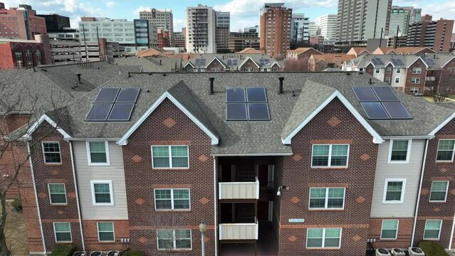 Small solar panel arrays on top of residential apartments in American city. Aerial rising shot of housing with self sufficient sustainable energy photovoltaic cells.