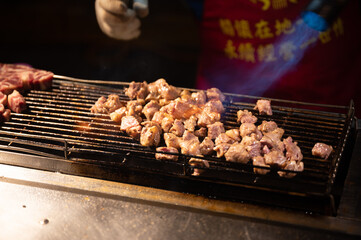 Closeup of pieces of freshly cut and chopped red meat on barbeque for grill with hot top fire gun throwing flame on the delicious food