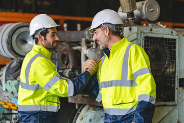 Two senior male engineers and workers wearing safety vests and jacket along with hardhat or helmet while clenching hands and making a fist standing in front of machine in warehouse