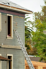 House undergoing repairs on roof and windows with blue wooden facade and white accent paint with ladder