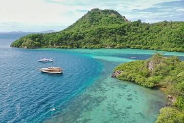 Idyllic panorama of a bay in Komodo National Park on Flores with turquoise sea with boats and green hills.