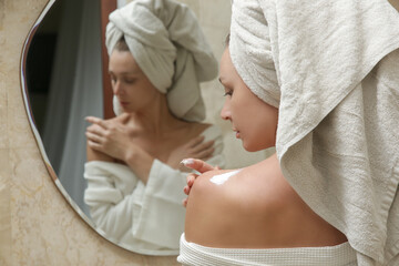 Woman applying body lotion to moisturize her skin after shower, beauty skin care concept	