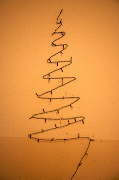 Ausgeschaltete alte Lichterkette in Form eines Weihnachtsbaums hängt trostlos an einer Wand mit alter Tapete