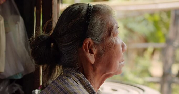 Asian female farmer who is a poor elderly native looking through the old narrow window, Used in humanity, documentary, lonely person, environment concepts or movies concept.