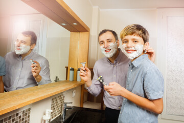 Father with kid shaving together holding razor in bathroom