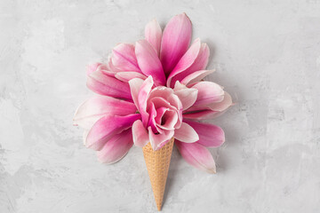 Ice cream cone with pink magnolia flowers on concrete background. Spring holiday concept. Flat lay....
