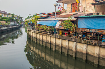 Fototapeta na wymiar A klong or river channel with fishing boats, buildings and house fronts in Thailand Asia