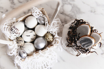 Painted silver and white Easter eggs on a light background and cake, postcard, free space for text, selective focus
