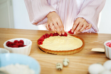 Obraz na płótnie Canvas Chef Woman decorating cake with berries and cream cheese on kitchen table. Close-up of female hands cooking tartlet with fresh raspberries