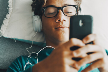 Serene young boy chatting and writing on mobile phone at home laying at bed. One teenager having relax indoor with cell smartphone app playing activity. Online dating modern teenager social media