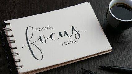 FOCUS FOCUS FOCUS. black lettering in notebook with cup of espresso and pens on black wooden desk - obrazy, fototapety, plakaty