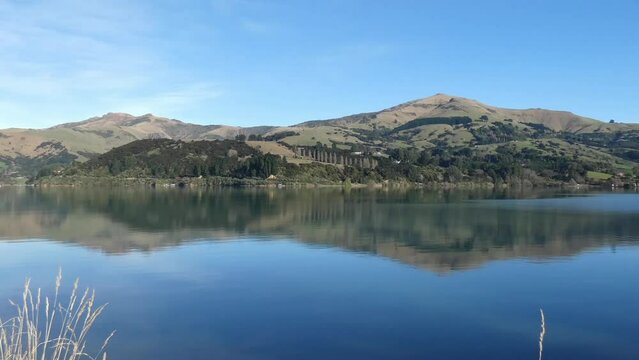 Ripples of water flow slowly across reflection of hills on a clear, calm morning - French Farm Bay, Akaroa Harbor (New Zealand)