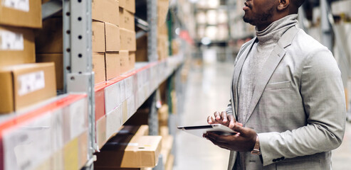 Portrait of smiling african american engineer man order details on tablet checking goods and supplies on shelves with goods background in warehouse.logistic and business export