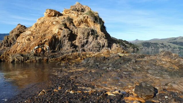 Sea water gently laps beside trachyte and basalt volcanic rock formations - Onawe Peninsula, Akaroa Harbor (New Zealand)