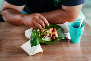 Nasi lemak wrapped in banana leaf with brown paper with people eating in the background.