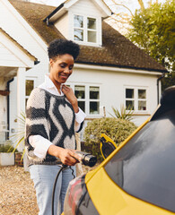 Woman charging electric car on driveway outside home