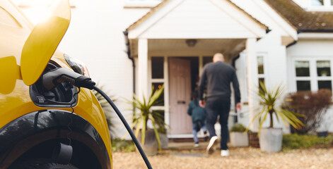 Electric car charging on driveway outside home with family in background
