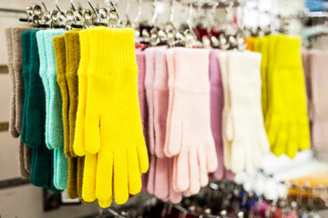 beautiful multi-colored knitted woolen gloves on hangers in the store, horizontal