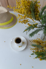 Spring still life, coffee, hat, mimosa on a white and wooden background