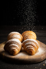 Upper view of four croissants on table with sugar falling, selective approach, black background, vertical