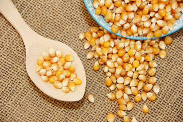 small grains of natural yellow dry corn in a decorative plate and in a wooden spoon on a rag jute brown background