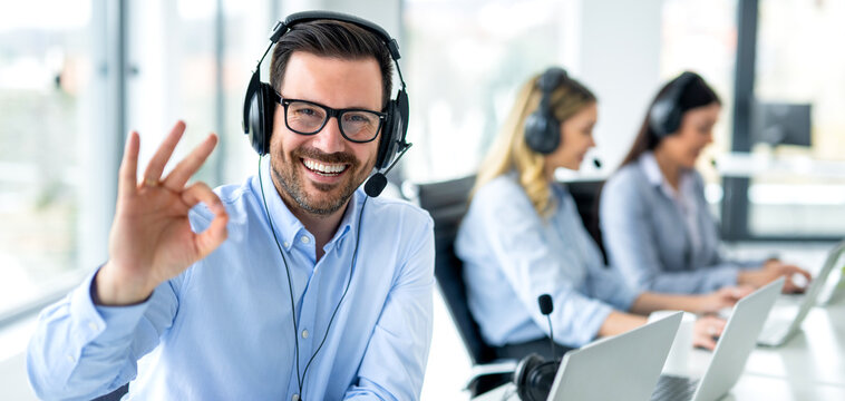 Panoramic view of handsome customer service representative showing approval sign to camera, smiling and gesturing okay at call center.