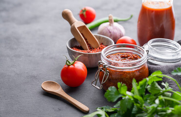 Homemade tomato sauce for pizza or pasta in a jar on a gray background with fresh vegetables, herbs and spicy. The concept of classic Italian cuisine.