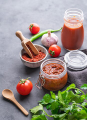 Homemade tomato sauce for pizza or pasta in a jar on a gray background with fresh vegetables, herbs and spicy.