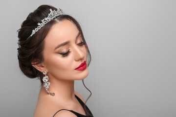 Beautiful young woman wearing luxurious tiara on light grey background, space for text