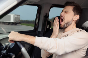Sleepy man yawning while driving his car
