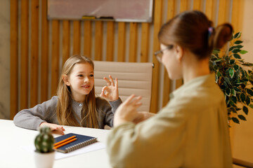 Happy smiling deaf little girl talking sign language with mute teacher.