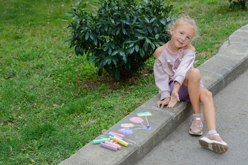 Little child sitting near drawn balloons and ukrainian flag with chalk on curb outdoors, space for...
