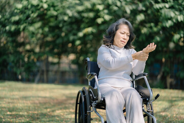 Fototapeta na wymiar Elderly patient sitting in a wheelchair outdoor, wrist pain.