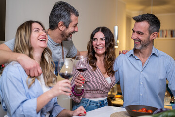 Dinner with friends at home, people toasting and having fun while cooking and preparing food