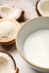Bowl of delicious coconut milk, flakes and coconuts on white table
