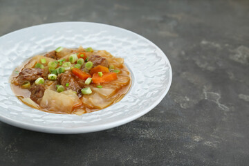 Tasty cabbage soup with meat, green onion and carrot on grey table, closeup. Space for text