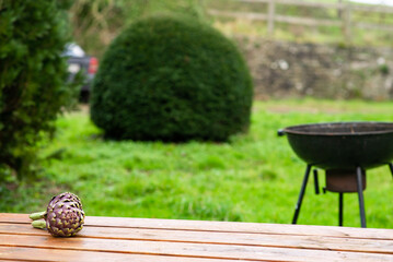 Artichoke on a wooden table outdoors on a blurred grill background. Preparing to cook green grill.