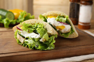 Delicious pita sandwiches with chicken breast and vegetables on wooden table, closeup