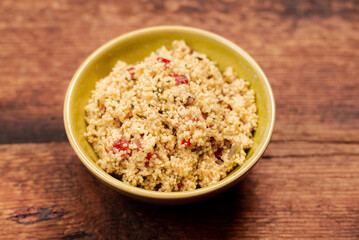 tabbouleh salad of couscous, spices and tomato - in a yellow plate on a wooden background. Traditional oriental salad, appetizer.