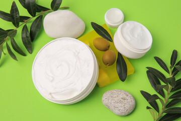 Different cosmetic products with olives and stones on light green background, above view