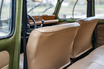 Lateral rear view of the interior of an old car with beige front seats, gear knob and steering wheel