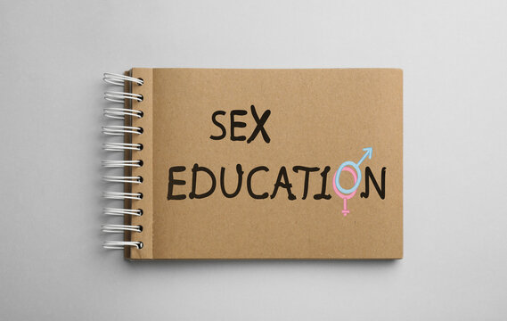 Text Sex Education with female and male gender signs instead of letter O in notebook on light background, top view