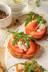 Bruschetta with tomatoes, arugula, olive oil and cheese on white tray on textured background close up. Fresh italian toasts