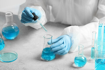 Fototapeta premium Scientist dripping liquid from pipette into beaker at white table, closeup