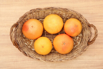 Wicker basket with fresh ripe grapefruits on wooden table, top view