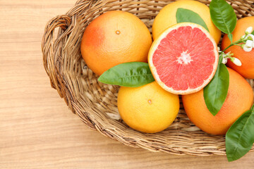 Wicker basket with fresh ripe grapefruits and green leaves on wooden table, top view
