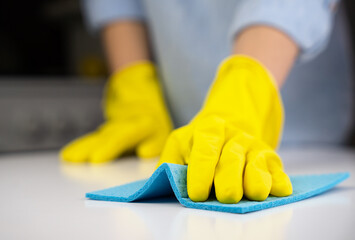 Woman in yellow rubber gloves wipes the dust on the table with a rag. Housekeeping concept. Close-up. Selective focus.