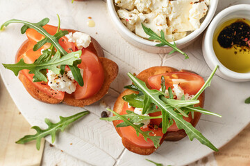 Bruschetta with tomatoes, arugula, olive oil and cheese on plate on textured background close up. Fresh italian toasts top view